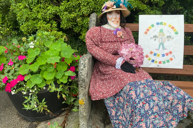 A Bere in Bloom seated scarecrow lady with bunch of flowers.