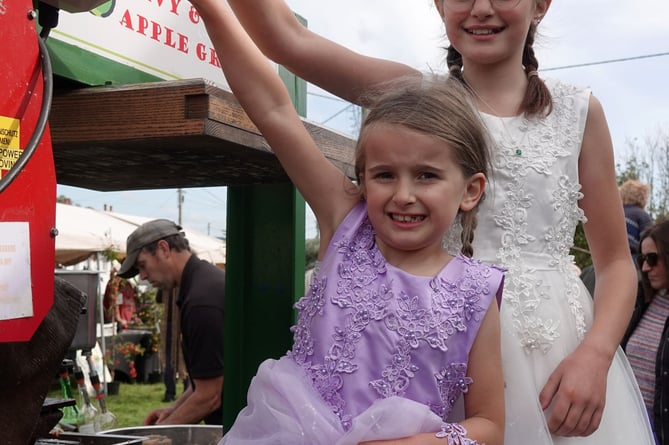 Carnival queen and attendant Ruby and Amber Perkin press the starter button on the apple crusher