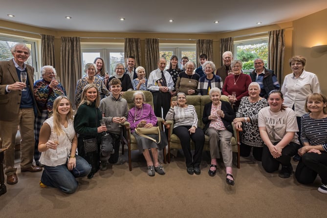 Residents, staff, and volunteers with Edward in the centre of the group proudly holding his birthday card from the King and Queen together with his daughter Jo on his left and grandsons Magnus and Alec, son Nick on his right and front left daughter-in-law Julie with grandchildren Nichole and Agnus.
