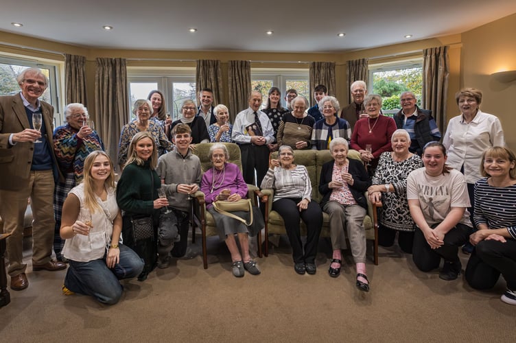 Residents, staff, and volunteers with Edward in the centre of the group proudly holding his birthday card from the King and Queen together with his daughter Jo on his left and grandsons Magnus and Alec, son Nick on his right and front left daughter-in-law Julie with grandchildren Nichole and Agnus.
